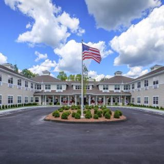 A large building with an American flag in front, surrounded by a landscaped circular driveway under a partly cloudy sky.