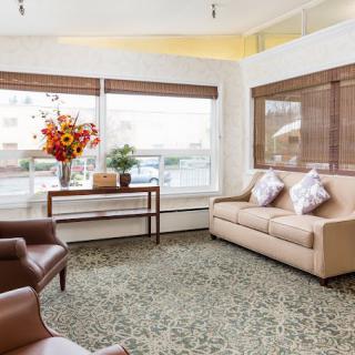 A cozy living room with a beige sofa and armchairs, complemented by a floral arrangement on a wooden table near large windows.