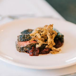 A beautifully plated dish featuring succulent beef, garnished with crispy elements and surrounded by a rich sauce.