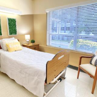 A well-lit hospital room featuring a patient bed, chair, and large window.