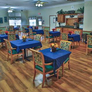 A cozy dining room with blue tablecloths and floral arrangements on each table.