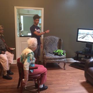 Two elderly individuals playing a video game under the guidance of an instructor.