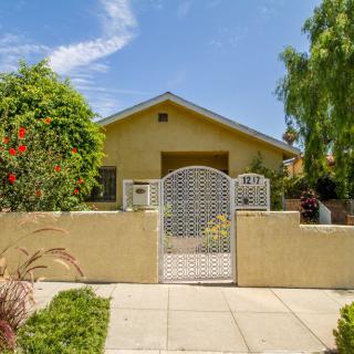 A charming house with a fenced front yard and lush greenery under a clear blue sky.