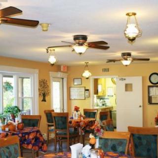 A cozy dining room with multiple ceiling fans, tables set for meals, and warm lighting.