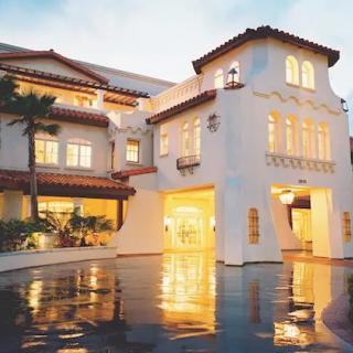 A luxurious hotel building illuminated in the evening, with its lights reflecting on a glossy surface.