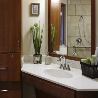 A modern bathroom with a wooden cabinet, mirror, and a neatly organized countertop featuring a vase with plants.