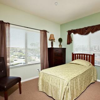A cozy bedroom with a single bed covered in green bedding, surrounded by large windows with curtains.