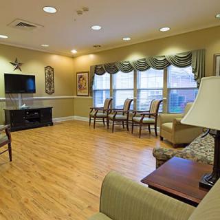 A cozy and well-lit living room with modern furnishings, featuring a television, sofa, chairs, and wood flooring.