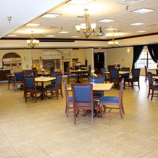 An empty dining room with tables and chairs arranged neatly, featuring chandeliers.