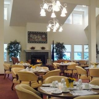 A well-lit dining room with neatly arranged tables and chairs, featuring a chandelier and a fireplace.