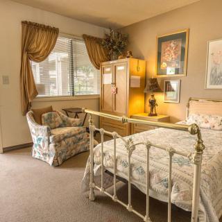 A cozy vintage-style bedroom with an ornate bed, armchair, cabinet, and window with curtains.