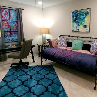 A cozy bedroom with a daybed, desk, and vibrant artwork.