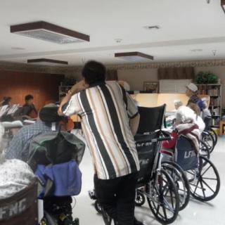 A caregiver assists elderly individuals in wheelchairs at a nursing home's community room.