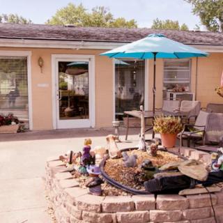 A cozy backyard patio with a blue umbrella and comfortable seating, surrounded by a small garden.
