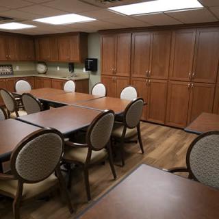 A conference room with wooden tables and upholstered chairs, featuring ample cabinet storage and fluorescent lighting.