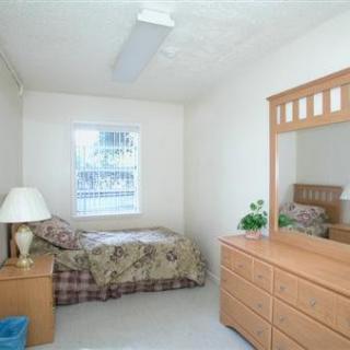 A minimalist bedroom with a single bed, dresser with mirror, and a lamp.