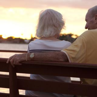 An elderly couple sits on a bench, enjoying a peaceful sunset by the lake.