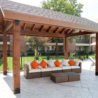 A cozy outdoor seating area under a wooden pergola with bright orange cushions.