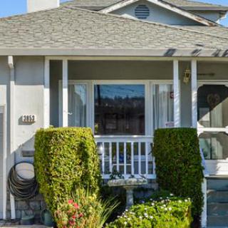 A charming residential house with a small porch and neatly trimmed bushes in the front yard.