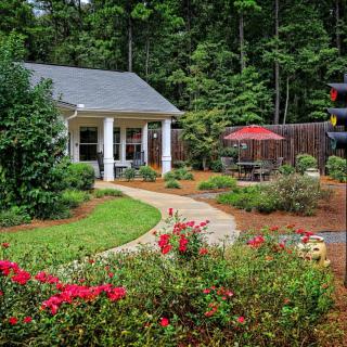 A beautifully landscaped garden with a cozy house, featuring a pathway, vibrant flowers, and outdoor seating under an umbrella.