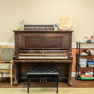A classic upright piano with a padded bench, surrounded by a bookshelf and wall decorations in a cozy music room.