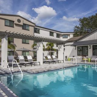 A serene outdoor pool area at a hotel, featuring lounge chairs and a pergola under a clear blue sky.