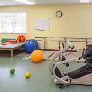 A rehabilitation room equipped with exercise balls, a stationary bike, and parallel bars for physical therapy.
