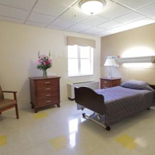 A well-lit hospital room with a single bed, dresser, and chair.