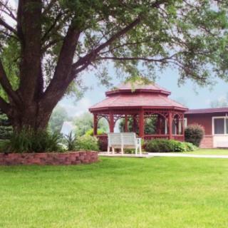 A peaceful outdoor scene with a gazebo, bench, and well-maintained lawn under a large tree.