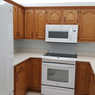 A corner kitchen with wooden cabinets, featuring a white oven and microwave.