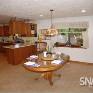A spacious kitchen and dining area with wooden cabinets and a central table beneath a decorative hanging lamp.