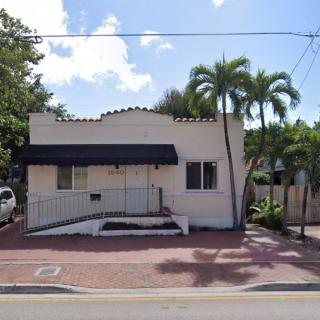 A small residential house with palm trees in the front yard, viewed from across the street on a sunny day.