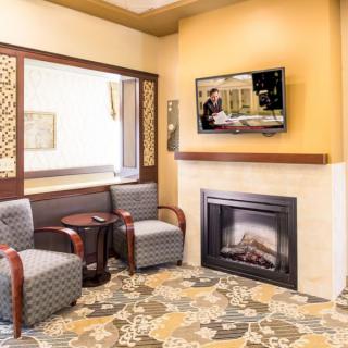 A cozy living room with a fireplace, two chairs, and a television on the wall.