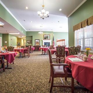 An elegant dining room with neatly arranged tables and chairs, decorated with red tablecloths and a central chandelier.