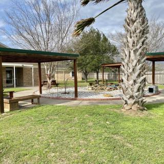 A peaceful outdoor patio area with wooden pavilions, surrounded by trees and grass.