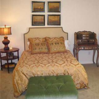 A cozy bedroom featuring a bed with decorative pillows, a side table with a lamp, artwork on the wall, and a small desk.