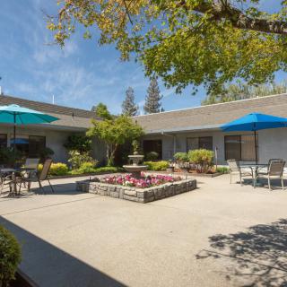 A peaceful courtyard with a central fountain, surrounded by outdoor seating and shaded areas.