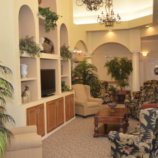 A cozy living room with elegant furniture and greenery, featuring built-in shelves and a television.