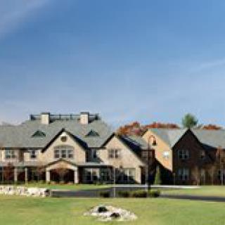 A large estate with a well-maintained lawn and multiple sections to the building, set against a clear blue sky.