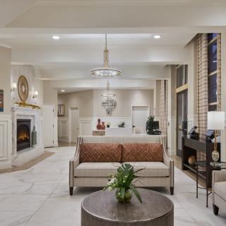 A modern living room with elegant decor, featuring a central sofa, a fireplace, and a chandelier.