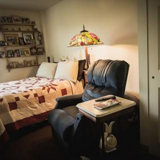 A cozy bedroom with a quilted bed, an armchair, and a decorative lamp.
