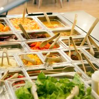 A self-serve salad bar with a variety of fresh vegetables and toppings.