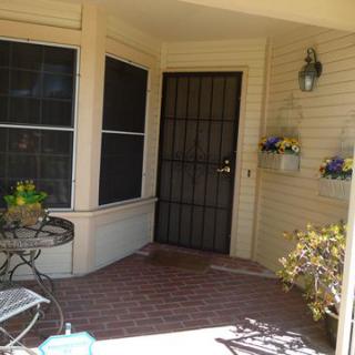 A welcoming front porch with a brick floor, featuring a wrought iron door and decorative plants.