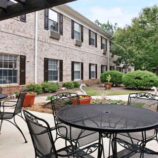 A tranquil outdoor patio area with tables and chairs, surrounded by landscaped greenery in front of a residential building.