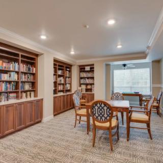 A cozy library with bookshelves, tables, and chairs in a well-lit room.