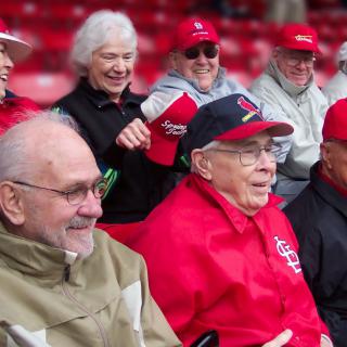 A group of elderly individuals enjoying a sports event, dressed in red attire and smiling.