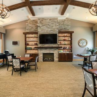 A cozy living room with a stone fireplace and modern decor, featuring wooden beams, chandeliers, and multiple seating areas.