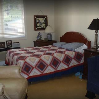 A cozy bedroom featuring a quilt-covered bed, wooden furniture, and a window allowing natural light.