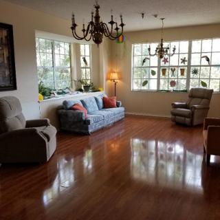 A cozy living room with a sofa, armchairs, and natural light streaming through large windows.