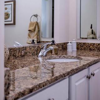 A bathroom with a granite countertop and sink, featuring a mirror and towel rack.